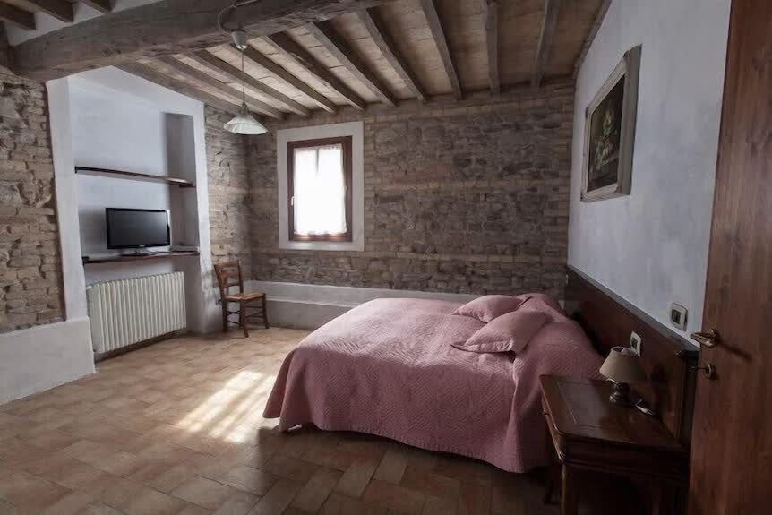 Camera matrimoniale in pietra a vista con soffitto a travi e letto rosa antico all'Agriturismo San Polo