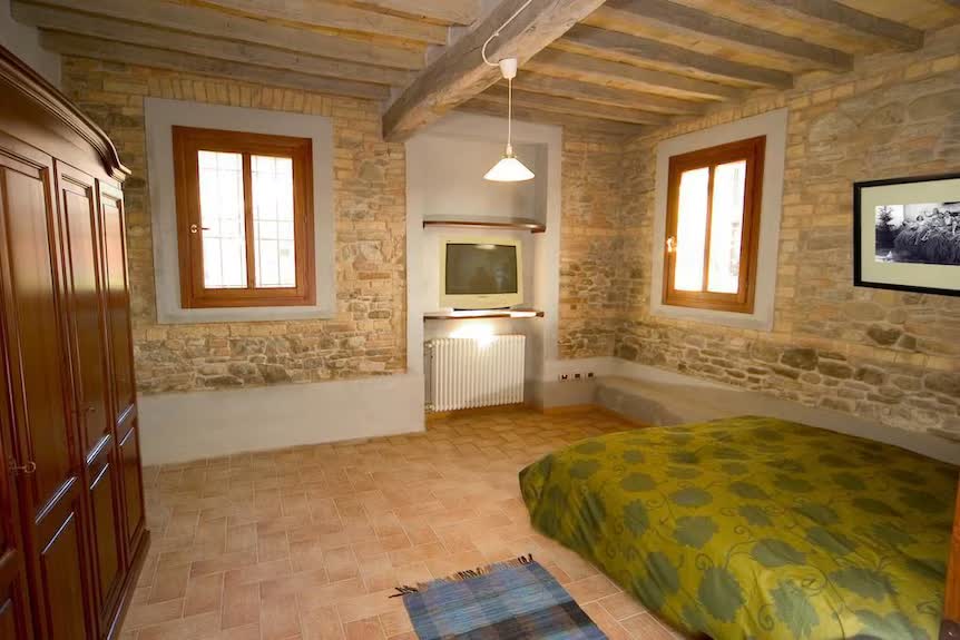 Camera dell'Agriturismo San Polo con muri in pietra, travi in legno e letto matrimoniale con copriletto a fiori